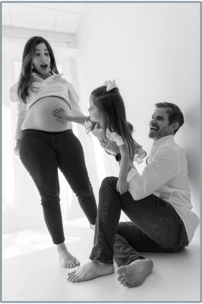 family of three with child holding a hand on moms belly