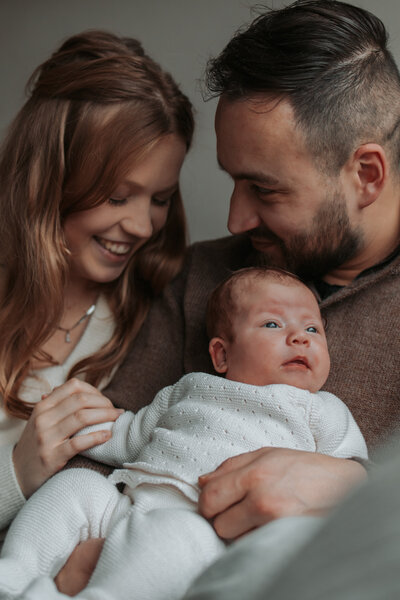 Een man en vrouw houden een baby vast en glimlachen naar de camera, stralend van geluk en liefde.