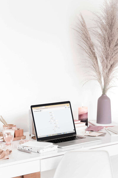 Laptop on a styled desk showing a HoneyBook systems website for wedding photographers, surrounded by notebooks, pampas grass, and candles.