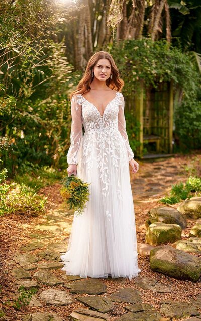 SHEER BOHO-STYLE WEDDING DRESS WITH BELL SLEEVES For the boho, ultra-romantic bride with a bit of a wild side, Style D3145 is your bridal match made in heaven! No traditional florals here–the laces on this gown take on a super organic, leaf-like design reminiscent of fresh ivy. The curved V-neckline beautifully highlights the upper body, while the leafy designs shower over the sheer bodice and become slightly more concentrated where you need the most coverage. This wide neckline extends into the long, voluminous sleeves of sheer fabric. Finally, the open V-back and short, manageable train show off your natural beauty and capture your effortless style perfectly.