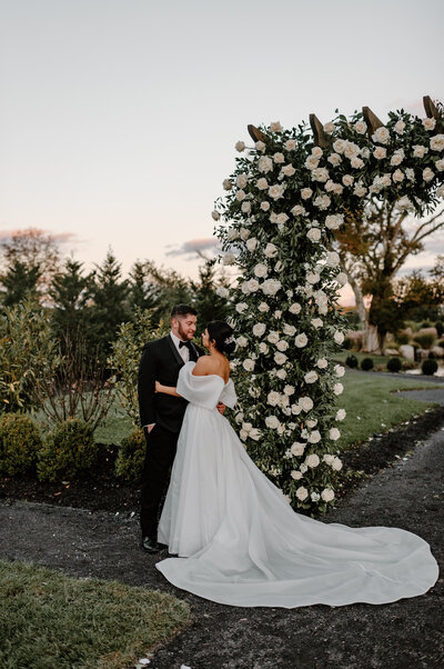 Tuscan inspired Renault winery wedding in Egg Harbor New Jersey.  Bride and Groom smile at each other in front of their floral wedding arch that they got married under.