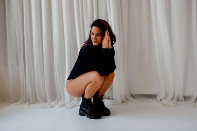 Emily Michele in a soft yet confident pose wearing a black bodysuit, symbolizing embodiment, empowerment, and inner liberation through shadow work.