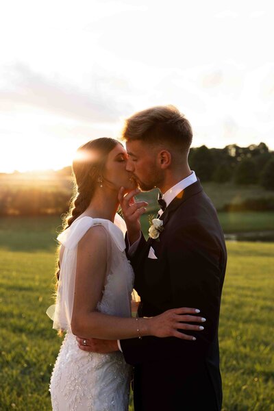 bride and groom kissing in front on sunset standing in a green field