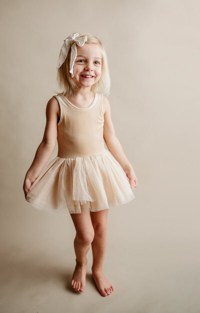 Little girl in beige tutu on a beige backdrop smiling for camera