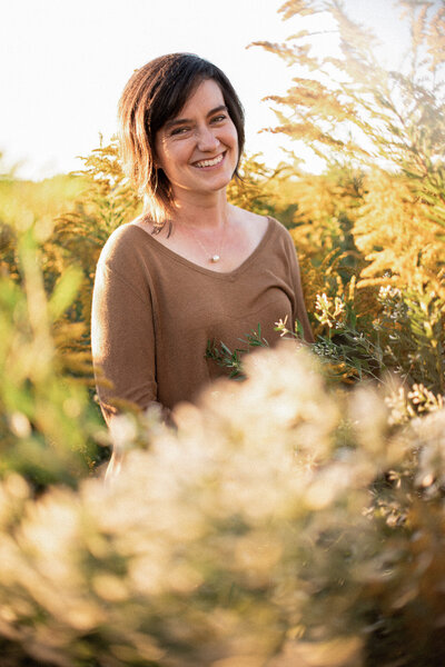 Stephanie, Denver wedding photographer smiles at the camera in a field of golden rod.