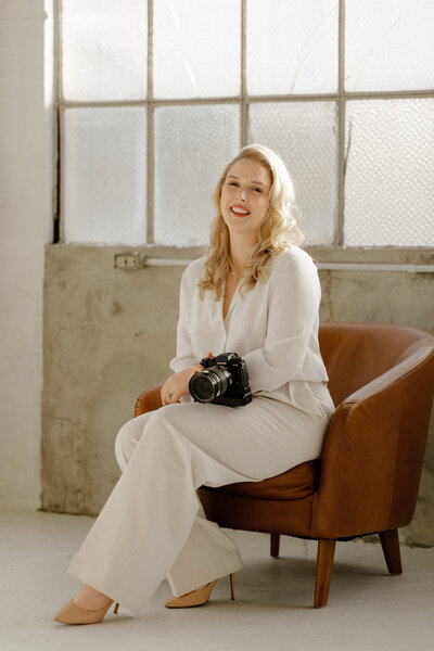 Woman sitting in sunlit studio laughing at camera