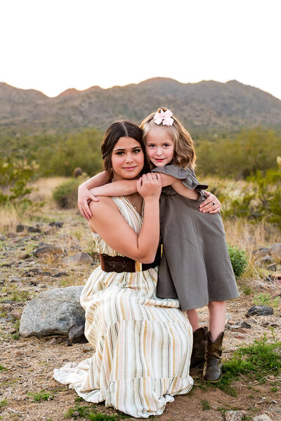 arizona mom with two daughters hugging her maternity belly in lake pleasant for photography session