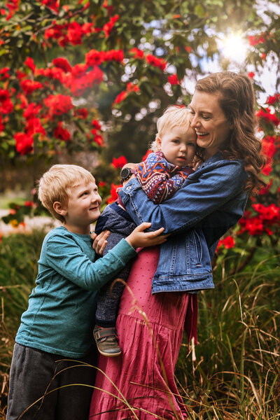 Vibrant and emotive lifestyle photograph of mother and children embracing in floral meadow