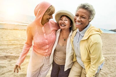 3 mid-age women  walking together on beach and smiling.