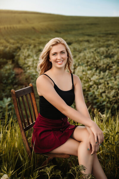This senior sits on a wooden chair in a field.