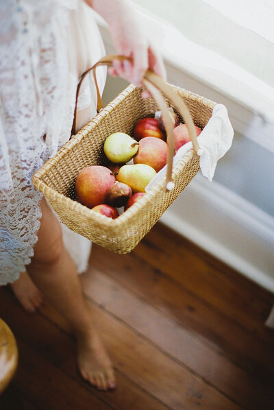 Barefoot woman tenderly carrying a rattan basket of foraged pears, apples and figs up the stairs
