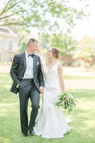 Bride and groom hold hands and look at each other.