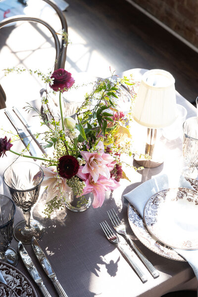 Shot of the end of a table, featuring a pastel pink, green and fuchsia bouquet, flanked by a placesetting in the corner. 