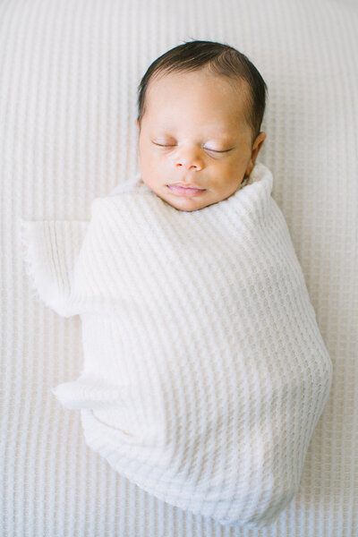 A baby wrapped in a white swaddle sleeping during his newborn photography session by Daniele Rose