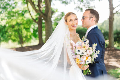 a bride smiles at the camera as veil swoops towards lens