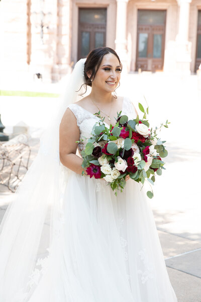 An Austin-based wedding photographer captures a stunning bride in her elegant wedding dress holding a beautiful bouquet in front of the majestic capitol building.