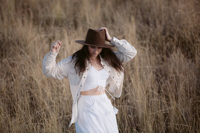 woman in a field holding her cowboy hat on her head