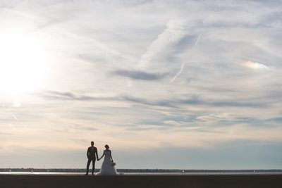 bride and groom holding hands on a pier at sunset