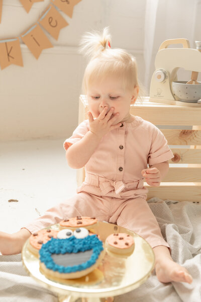 baby girl holds hand to mouth excitedly while looking down to decorated cookies on stand including cookie monster cookie at studio session in ann arbor michigan