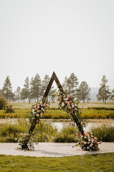 Triangle arch at Sunriver Resort Mt Bachelor lawn with peach, coral and white roses with greenery