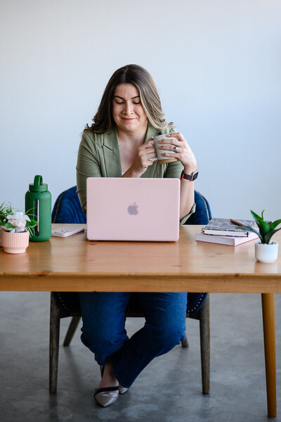 A small business owner sits at her desk sipping coffee and posing for her branding photos being taken by a Denver brand photographer and Denver commercial photographer