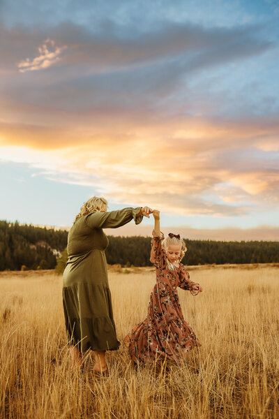 Mom and young daughter are twirling in the truckee mountains with a beautiful pink sunset