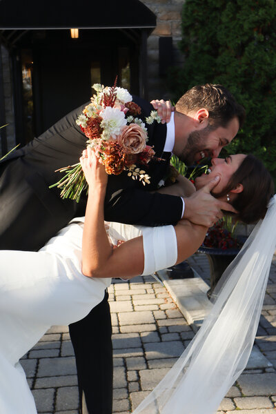 Newlywed couple embracing on stone steps outside restored 1890s schoolhouse at Ashlar Ottawa, showcasing outdoor ceremony space perfect for intimate micro weddings with up to 70 guests