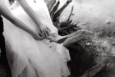bride sitting on a fallen tree trunk putting on her wedding shoes
