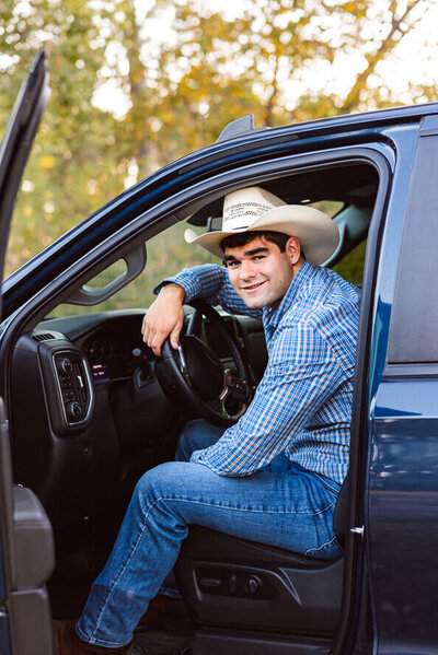 Boy with cowboy hat sit sin his truck for senior photos.