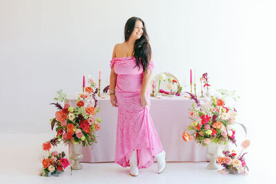 Woman in bright pink dress and white cowboy boots standing in front of a set table with elaborate floral arrangements around it