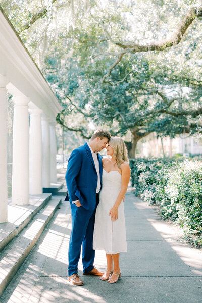 Engaged couple holding hands walking towards a white house