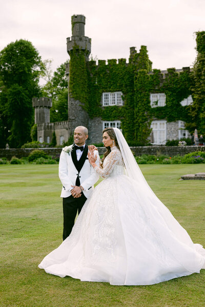 Candid photo of a newly wed couple with the groom wearing a white suit & the bride wearing a long flowing white dress in the gardens of Luttrellstown Castle
