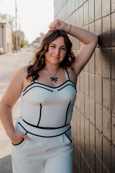 Girl in white leans against all black wall.