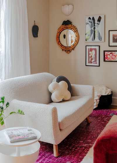 A white love seat with colorful rug beneath it and bright artwork on the wall representing colorful home decor.