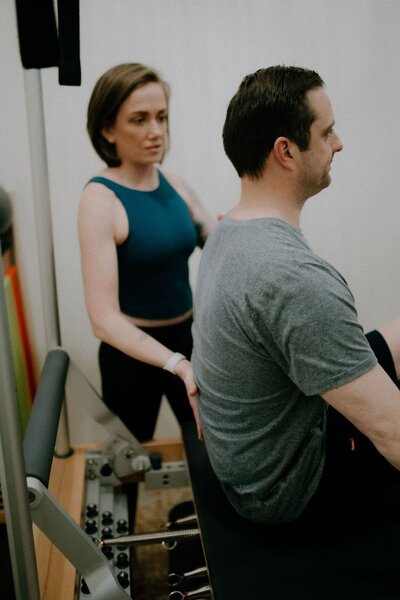 Brittany instructing a male pilates client through arm exercises on a Pilates refomer at Powerhaus Pilates studio in Powell Ohio