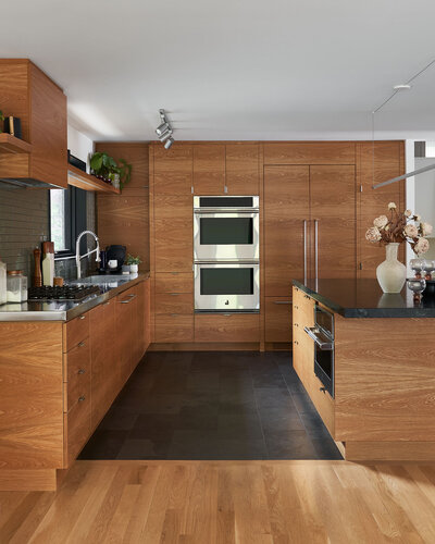 ChatGPT said:
A warm and modern kitchen featuring sleek wood cabinetry, integrated appliances, and dark stone countertops. A contrasting tile floor defines the workspace, while minimal decor and clean lines create a streamlined, functional feel. Subtle details like a glossy backsplash and natural light add depth and warmth.