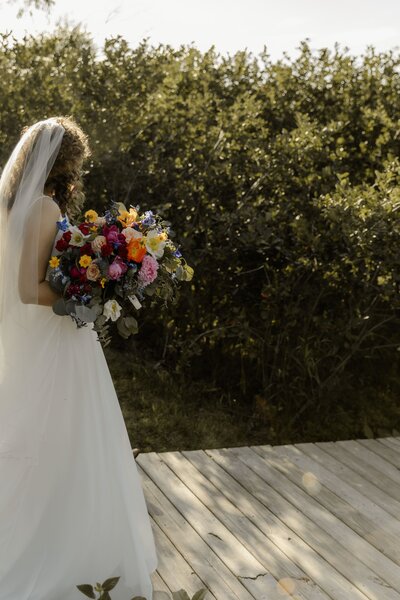 Candid moment of bride holding her colorful bouquet, backlit by the soft sun.