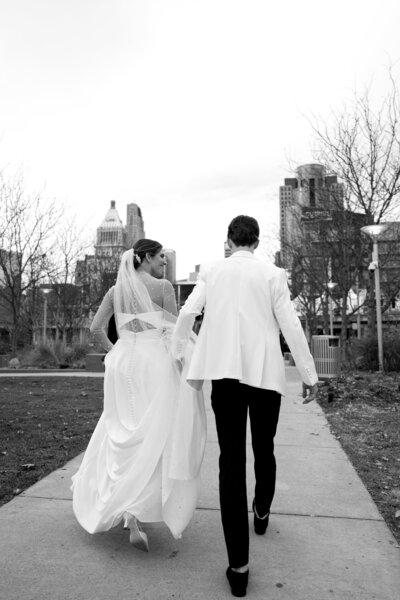 black and white photo of bride and groom running away from  camera