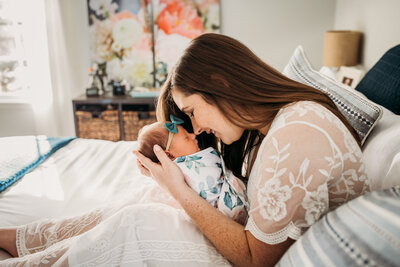 mom in a lace dress nuzzling newborn daughter with a floral painting in the background