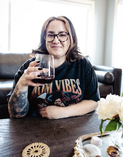 a woman in glasses sitting on the floor holding a glass of red wine