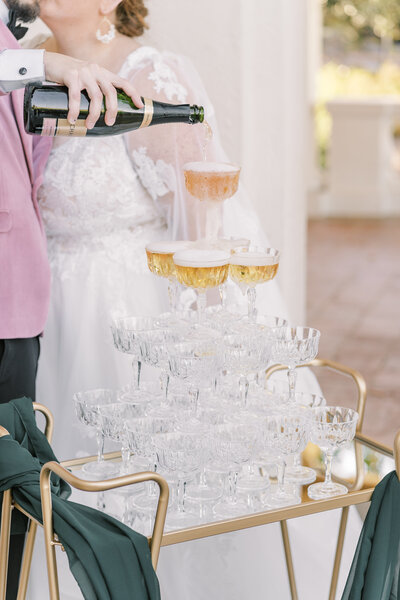 A bride and groom pour champagne over a champagne glass tower at their Villa Montalvo Wedding.