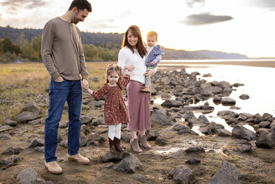 Candid outdoor family photo by a Portland, Oregon family photographer, showing parents and kids walking along a rocky riverbank at sunset.