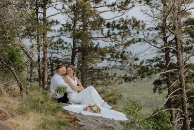 eloping couple snuggled together on a rocky overlook with pine trees in the background. captured by a north shore elopement photographer