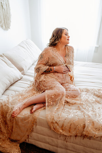 Maternity photography mother sitting on bed with hand draped over growing baby belly