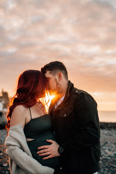 pregnant woman and her partner kissing during sunset on beach