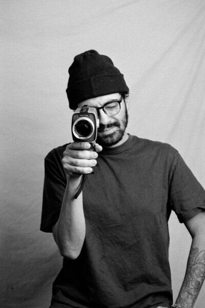 Black-and-white  portrait of one photographer with vintage cameras, wearing beanies and glasses. One holds a Canon film camera, the other a classic video camera, capturing timeless moments with an analog touch.