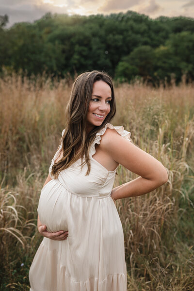 pregnant mother in pink silk maternity gown holding baby bump for maternity photoshoot in field
