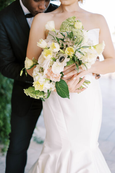 bride in a satin wedidng gown holding a beautiful  floral bouquet with white, yellow and  light pink florals in Tampa Bay Florida