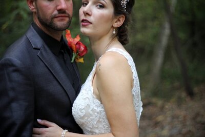 A bride and groom gaze at the camera as they stand bellies touching.