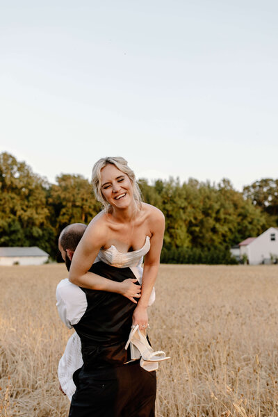 bride over grooms shoulder in field spinning and laughing while holding shoes photo